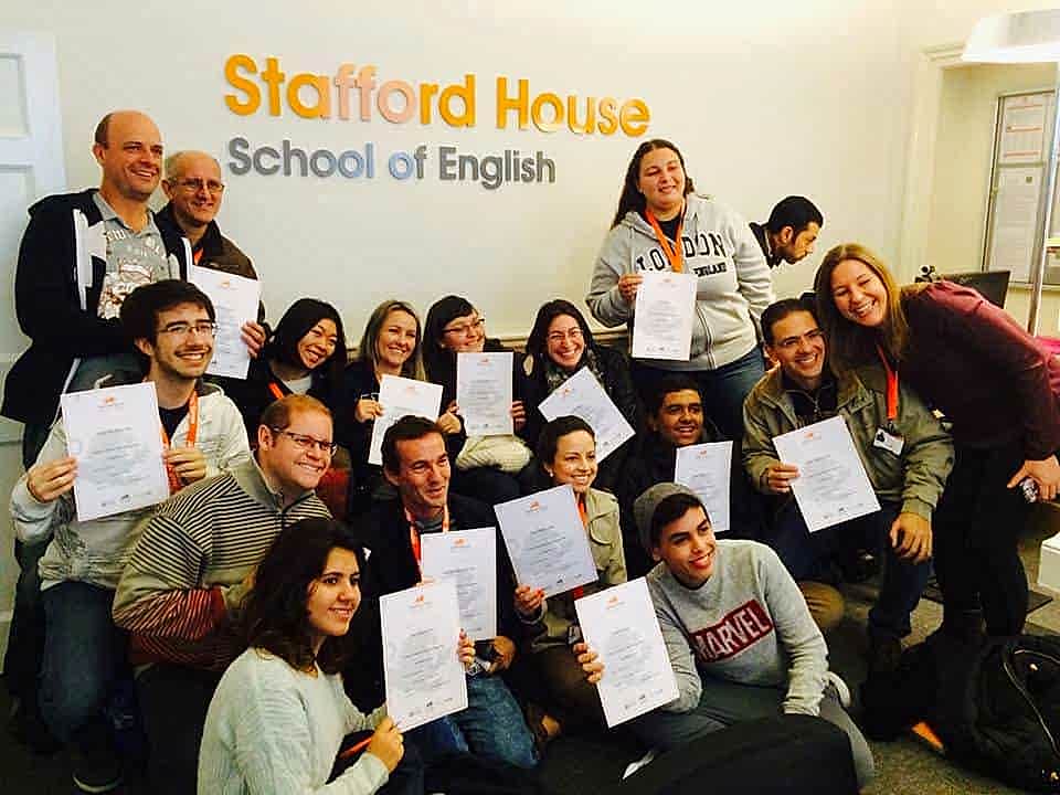 Students holding certificates in front of the Stafford House logo in London