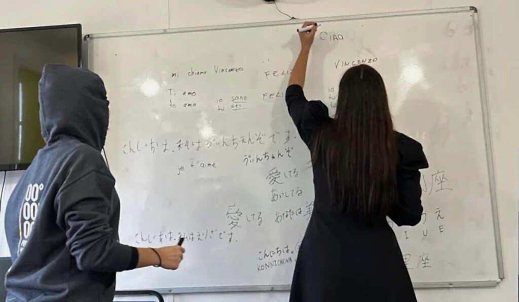 Students writing in different languages on a classroom whiteboard at Top Up Learning