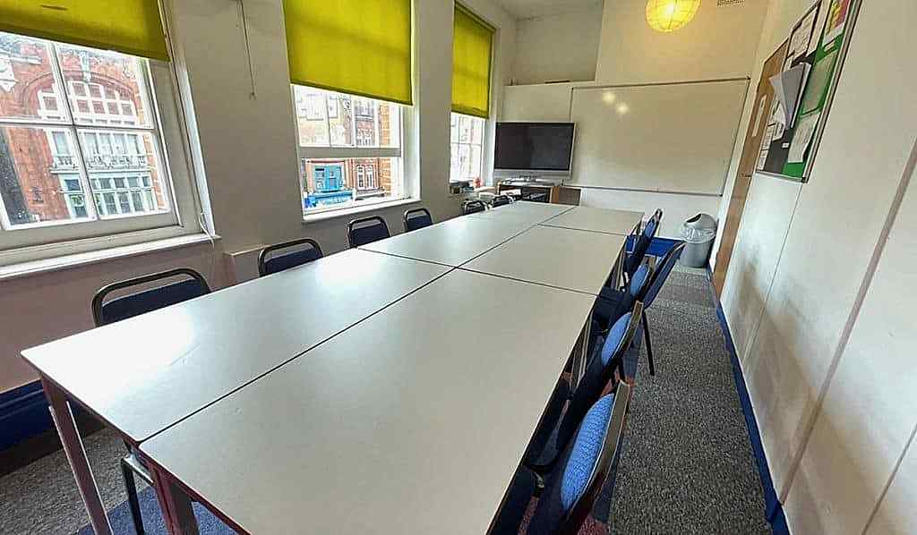 Empty classroom with long tables and blue chairs at Top Up Learning London
