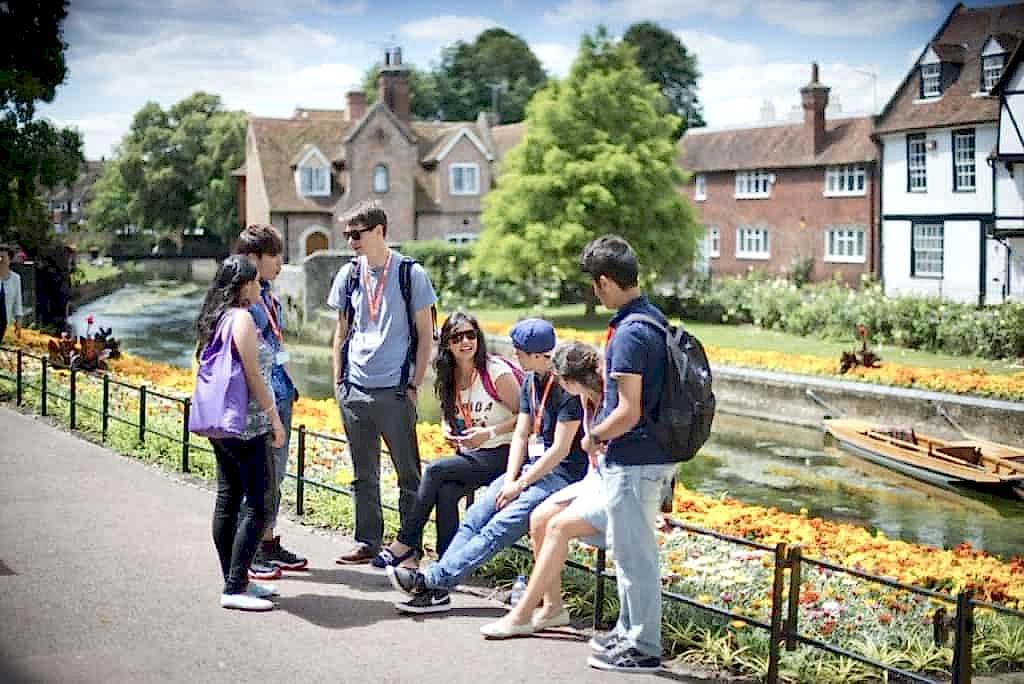 Students chatting beside a river and flower beds in Canterbury