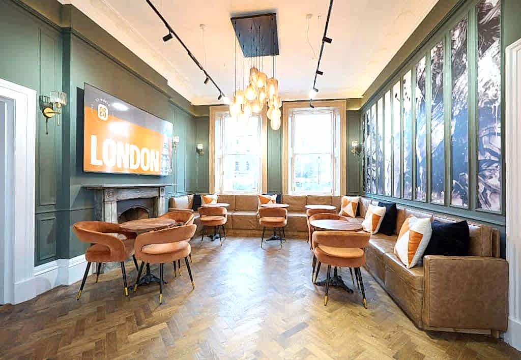 Student lounge with orange chairs, a sofa and a London sign at ES London