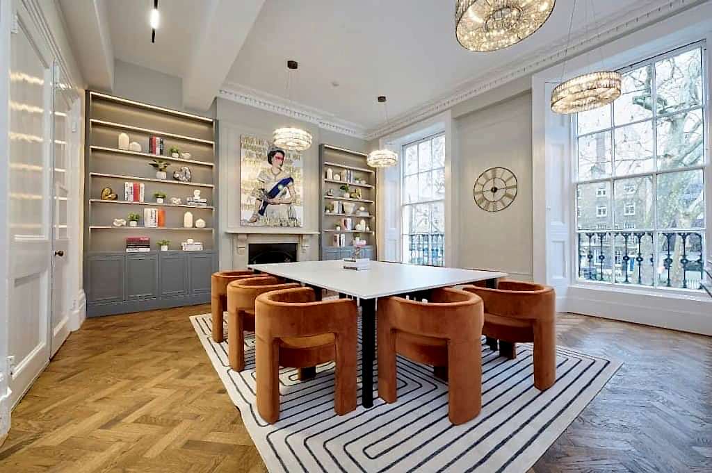 Meeting room with orange chairs around a white table and bookshelves at ES London