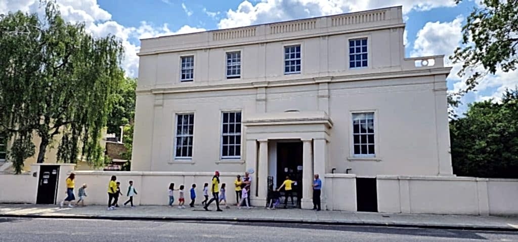 Children in yellow walking along the white front of Skola Gloucester Gate in London