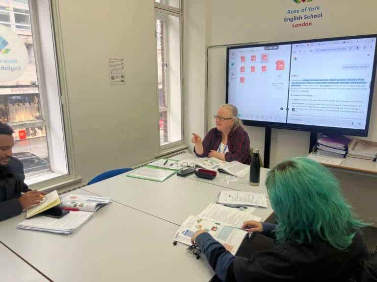 Teacher and students working from books beside a large screen at Rose of York