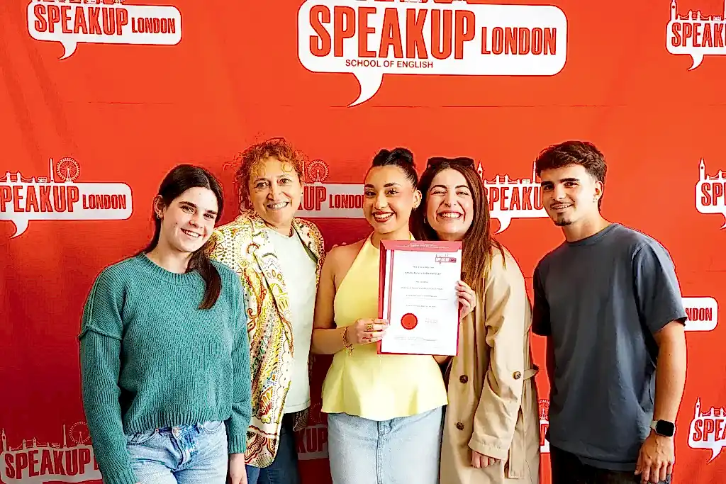 Speak Up London student receiving a certificate in front of the school's branded wall