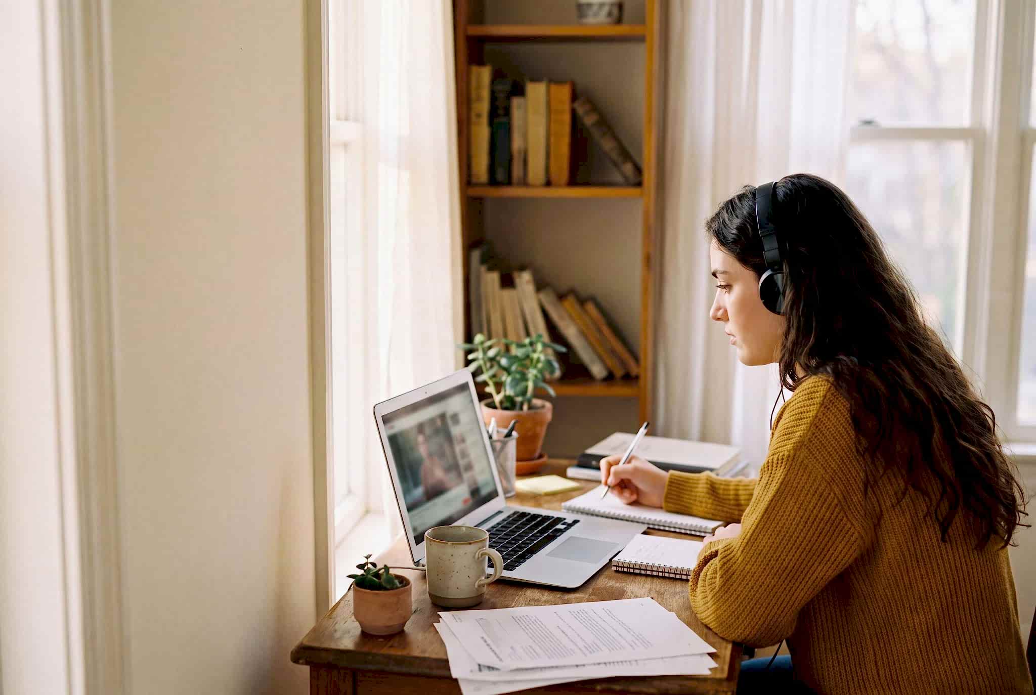 Student at home watching an IELTS video lesson on a laptop and taking notes